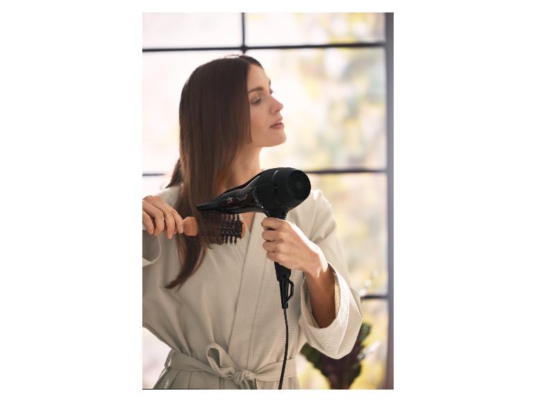 Frau föhnt sich die Haare mit einem Föhn und einer Rundbürste.