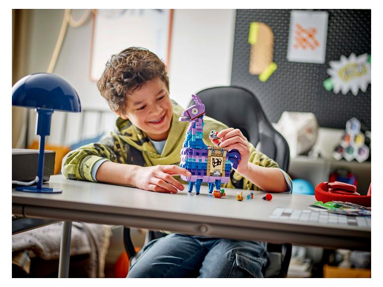 Ein lächelnder Junge spielt mit einer LEGO Fortnite Lama-Figur auf einem Schreibtisch.