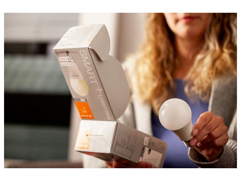 Frau hält Smart-Glühbirne und Verpackung mit „SMART+ LIGHTING“-Aufschrift