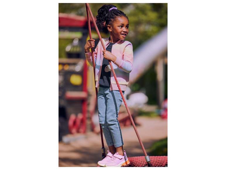 Ein Mädchen in einer rosafarbenen Bomberjacke und blauen Jeans steht auf einer Seilbrücke.