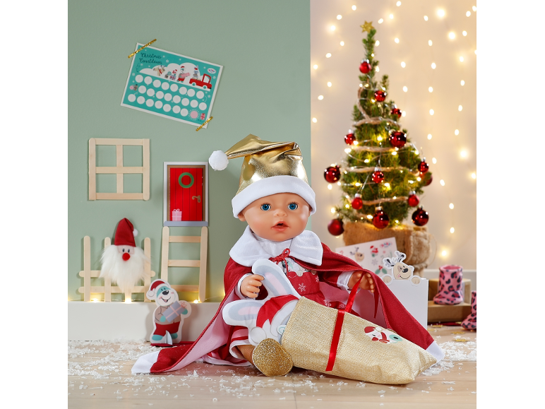 Babypuppe im Weihnachtskostüm mit Geschenksack vor festlichem Hintergrund.