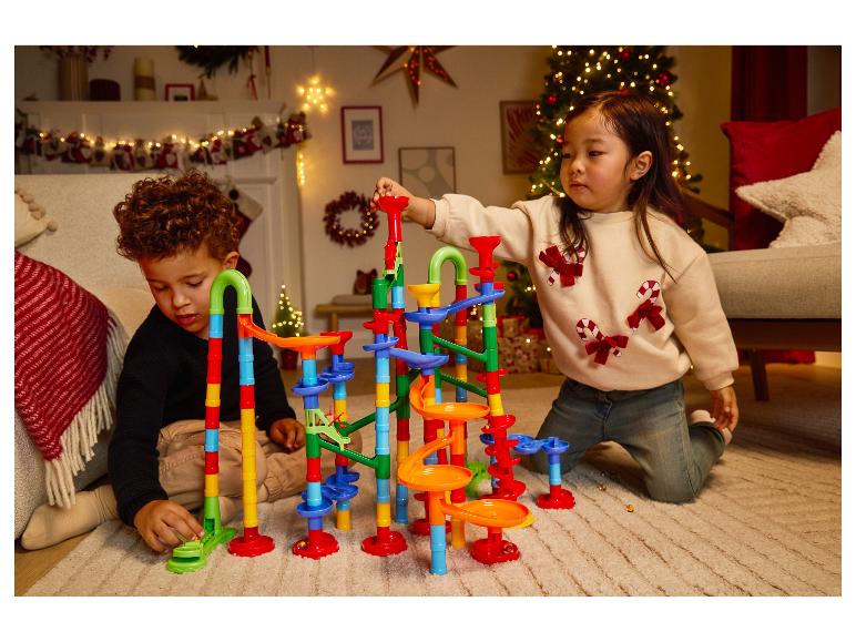 Zwei Kinder spielen mit einer bunten Kugelbahn auf einem Teppich in einem weihnachtlich dekorierten Raum.