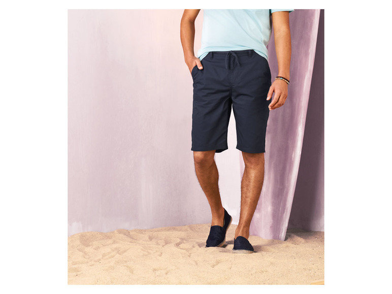 Mann in blauen Shorts und Sandalen am Strand.