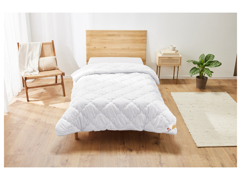 Eine weiße Bettdecke der Marke Polygiene auf einem Holzbettgestell.