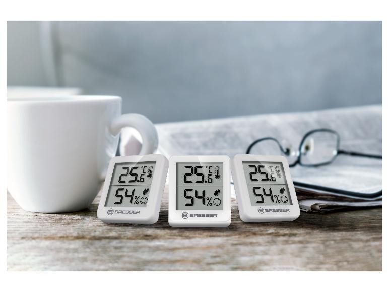 Drei weiße BRESSER Digital-Thermo-Hygrometer auf einem Holztisch.