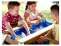 Kinder spielen mit einem Holzwassertisch mit blauen Behältern und Spielzeug.