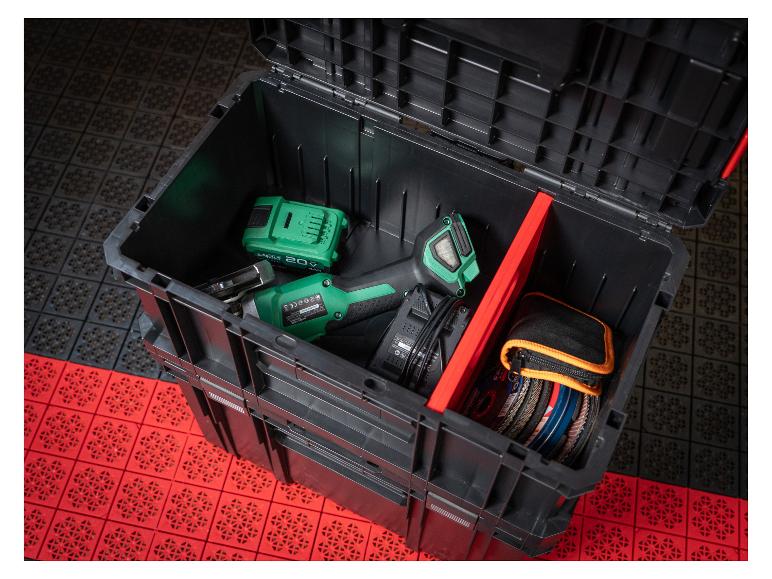 Offene Werkzeugkiste mit Elektrowerkzeug, Akku und Zubehör auf rotem und schwarzem Boden.