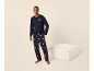 Mann in marineblauem Pyjama mit Teddybären, steht neben einem Pouf.