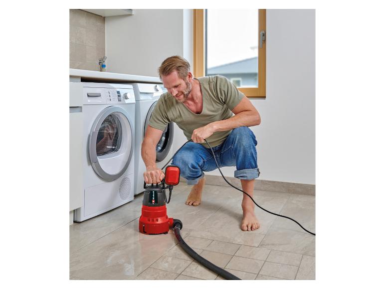 Mann benutzt eine Tauchpumpe, um Wasser vom Waschküchenboden zu entfernen.