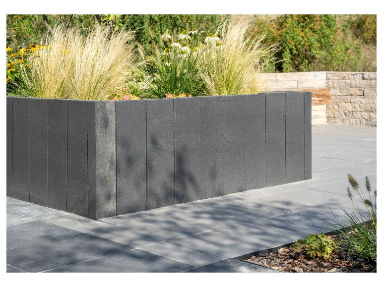 Dunkelgraues Betonblock-Pflanzgefäß mit Ziergräsern und Blumen.