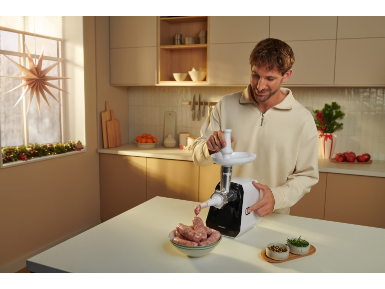 Mann in der Küche bereitet Würste mit einem Fleischwolf zu, Weihnachtsdekoration.
