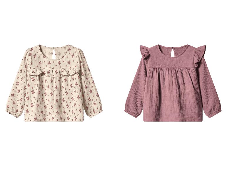 Zwei Kinderblusen, eine beige mit Blumenmuster und eine einfarbige rosa, beide langärmlig.