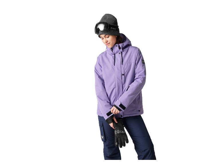 Frau in lila Skijacke, dunkelblauer Skihose, grauer Mütze und Skibrille.