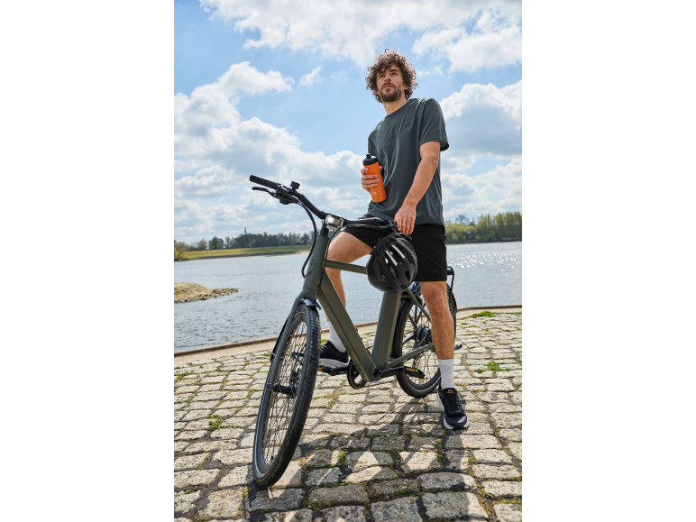 Mann auf einem Fahrrad am Wasser mit einer Trinkflasche in der Hand.