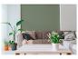 Wohnzimmer mit grüner Wand, grauem Sofa, Kissen, Decken, Pflanzen und weißem Couchtisch.