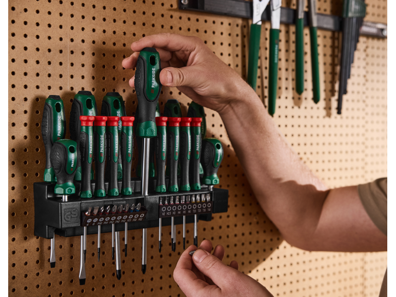 Eine Hand wählt einen Schraubendreher aus einem Set an einer Werkstatt-Lochwand.