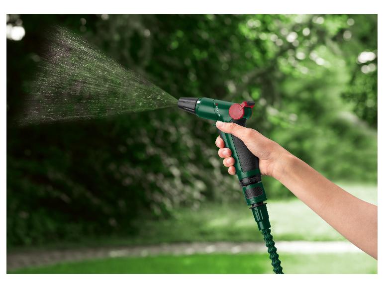 Hand hält grüne Gartenspritzpistole mit Wasserstrahl vor verschwommenem grünem Hintergrund.