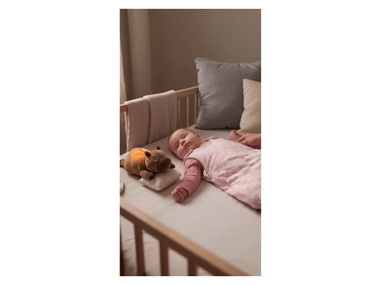 Baby schläft im Kinderbett in rosa Schlafsack mit leuchtendem Plüschtier.