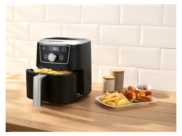 Schwarze Heißluftfritteuse mit Pommes und Hähnchenflügeln auf Holzarbeitsplatte.