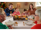 Familie am Weihnachtstisch versammelt, die auf einem Raclette-Tischgrill kocht.