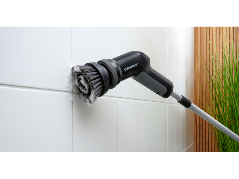 Elektrische Fliesenreinigungsbürste mit Schaum, vor Holzwand und Pflanzen.