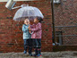 Zwei Kinder in Regenkleidung unter einem durchsichtigen Regenschirm.