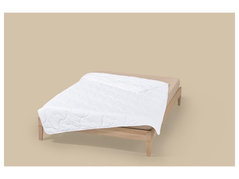 Bett mit weißer Steppdecke und beiger Bettwäsche auf neutralem Hintergrund.