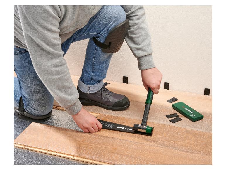 Mann verlegt Laminatboden mit Gummihammer und Abstandshaltern.