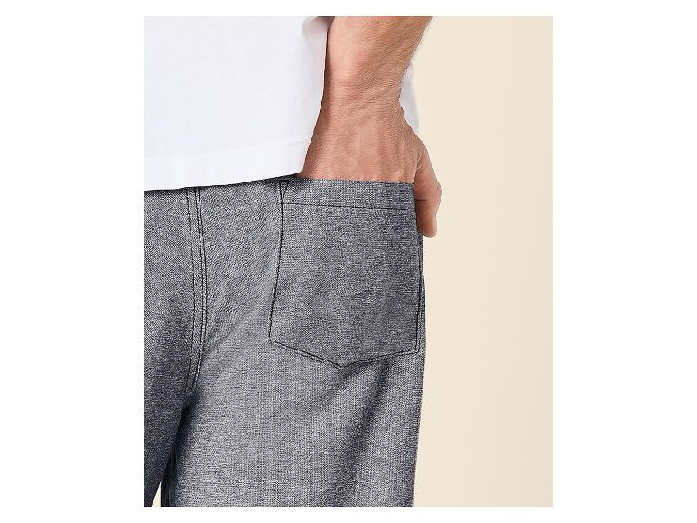 Mann in weißem T-Shirt und grauen Shorts, mit der Hand in der Tasche.