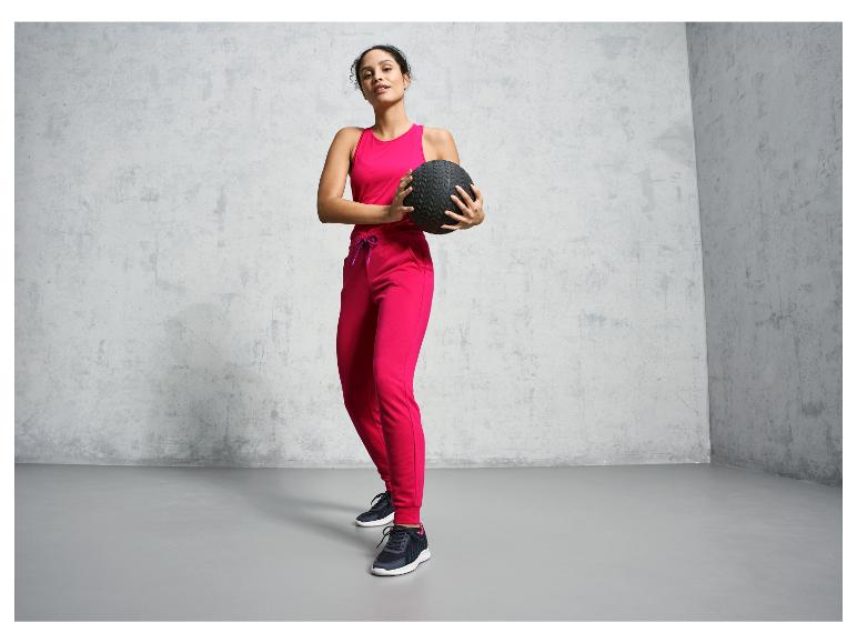 Frau in rosa Jogginghose und Top hält einen Fitnessball.