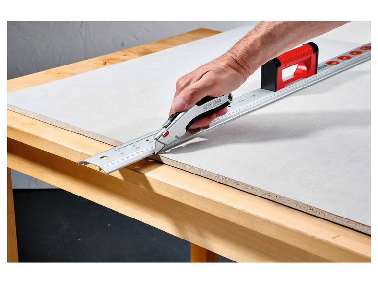 Eine Hand schneidet Holz mit einem Cuttermesser und einem Tackside-Lineal.