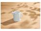 Weiße Keramik-Milchkanne auf einem hellen Holztisch mit gesprenkeltem Sonnenlicht und Schatten