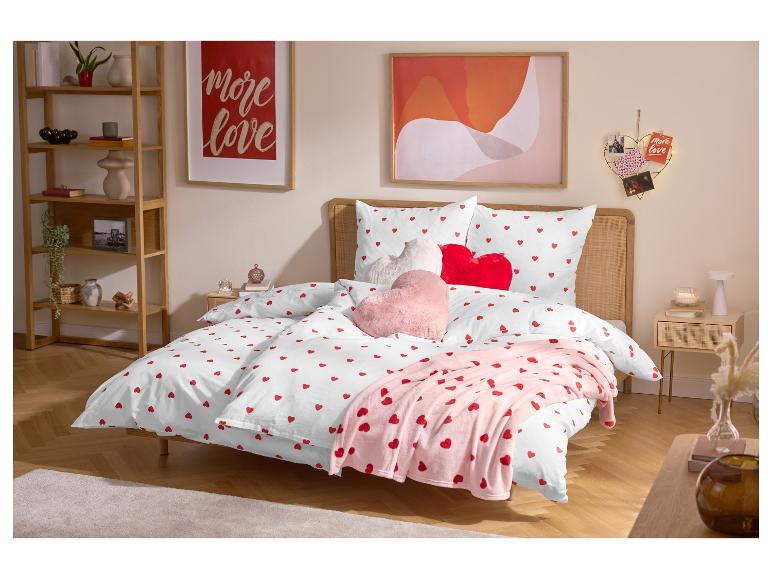Schlafzimmer mit Doppelbett, weißer Bettwäsche mit roten Herzen und herzförmigen Kissen.