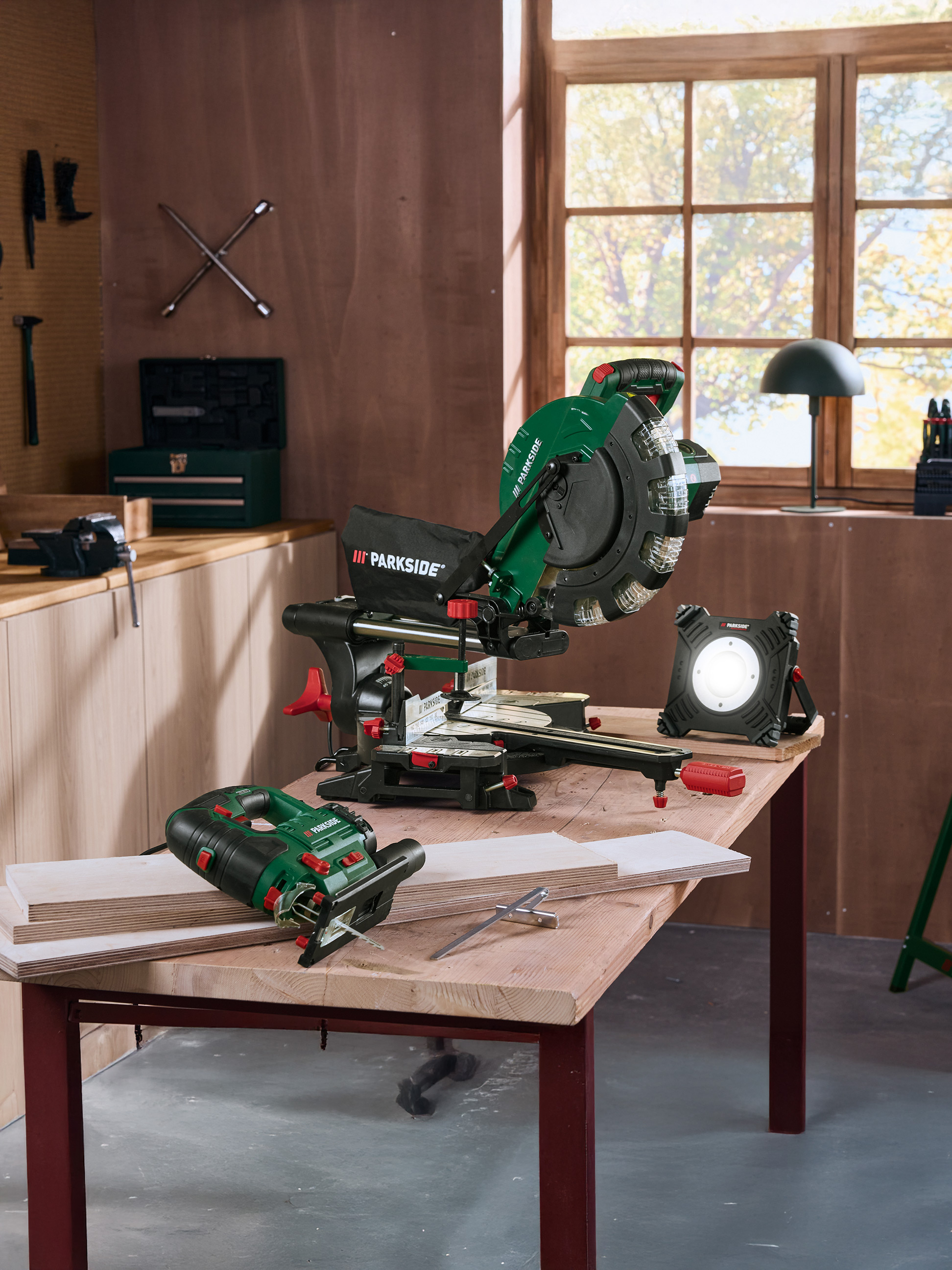 Parkside Werkzeuge: Kappsäge, Stichsäge und Arbeitsleuchte auf einem Holztisch in der Werkstatt.