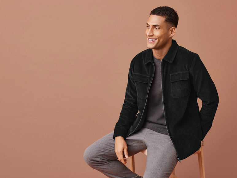 Mann in einer schwarzen Cordjacke und grauen Hosen.