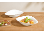 Rigatoni-Nudeln in einer weißen Schale, mit einer leeren Schale und einer Vorspeisenplatte.