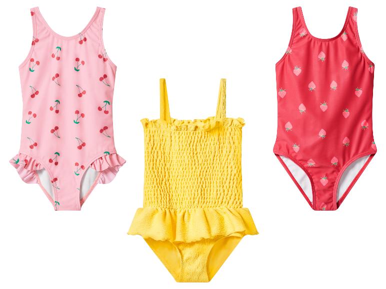 Drei Kinderbadeanzüge: rosa mit Kirschen, gelb mit Rüschen und rot mit Erdbeeren.