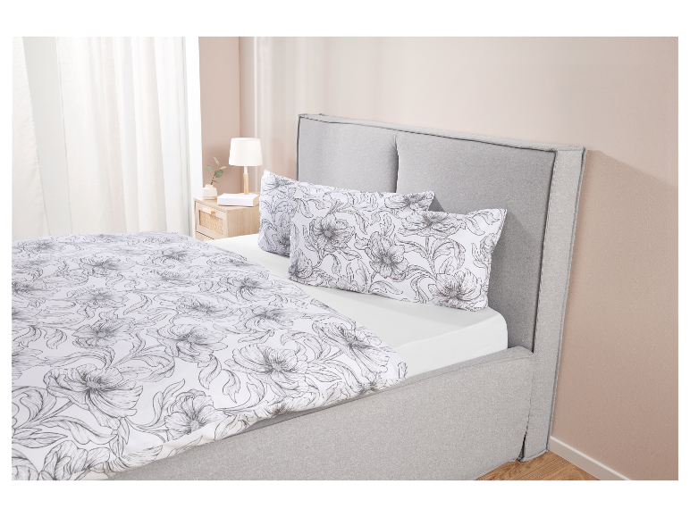 Blumige Bettwäsche in Weiß und Grau auf einem grauen Bett.