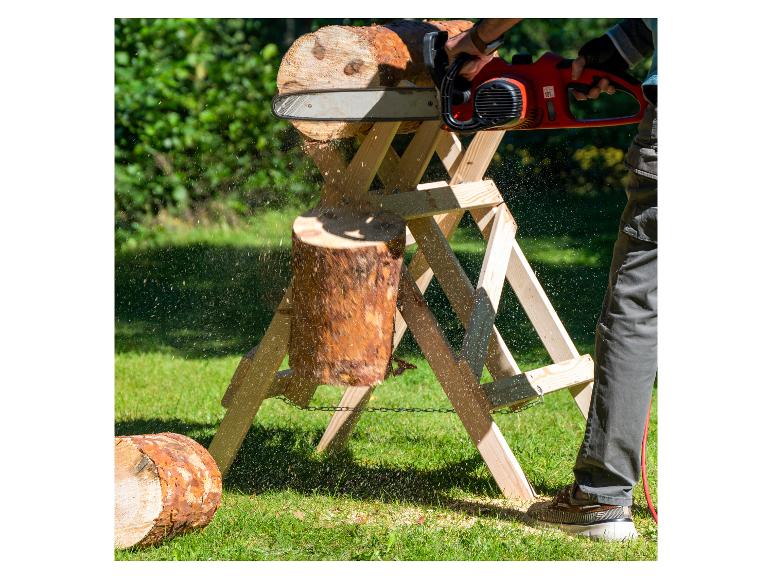Person schneidet einen Baumstamm mit einer Elektrokettensäge auf einem Holzsägebock im Garten.