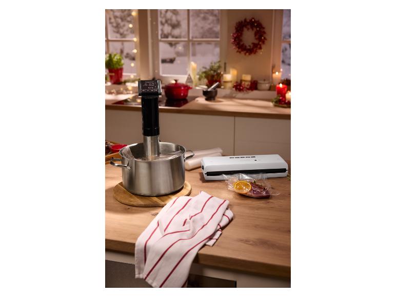 Sous-Vide-Garer in einem Topf, Vakuumiergerät und vakuumverpackte Lebensmittel auf einer Küchenarbeitsplatte.