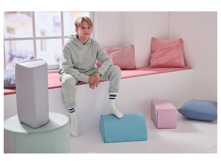 Ein Junge sitzt auf einer Fensterbank, umgeben von Kissen und bunten Poufs.