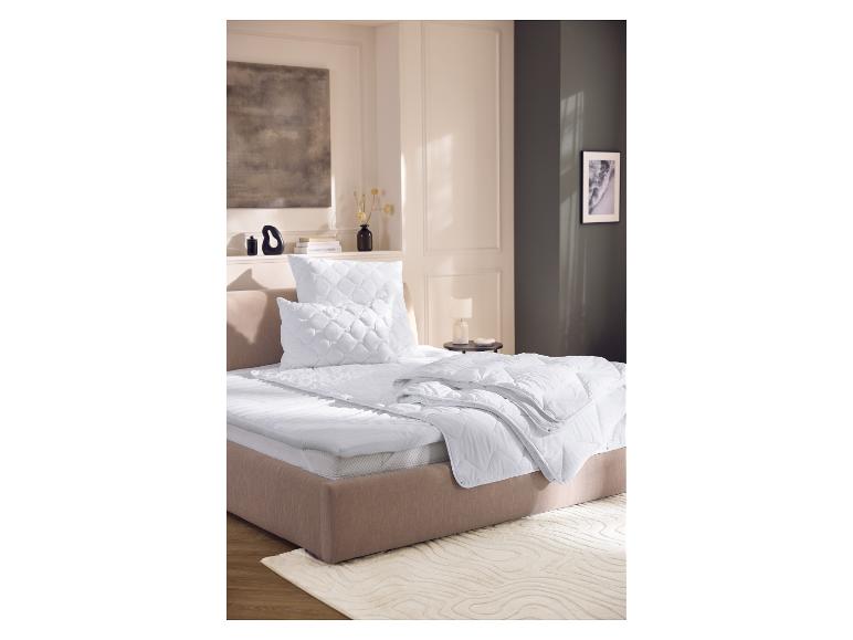 Bett mit weißer Matratze, Kissen und Decke in einem modernen Schlafzimmer.