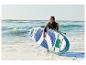 Frau mit Stand-Up-Paddle-Board und Paddel, im Wasser am Strand stehend.
