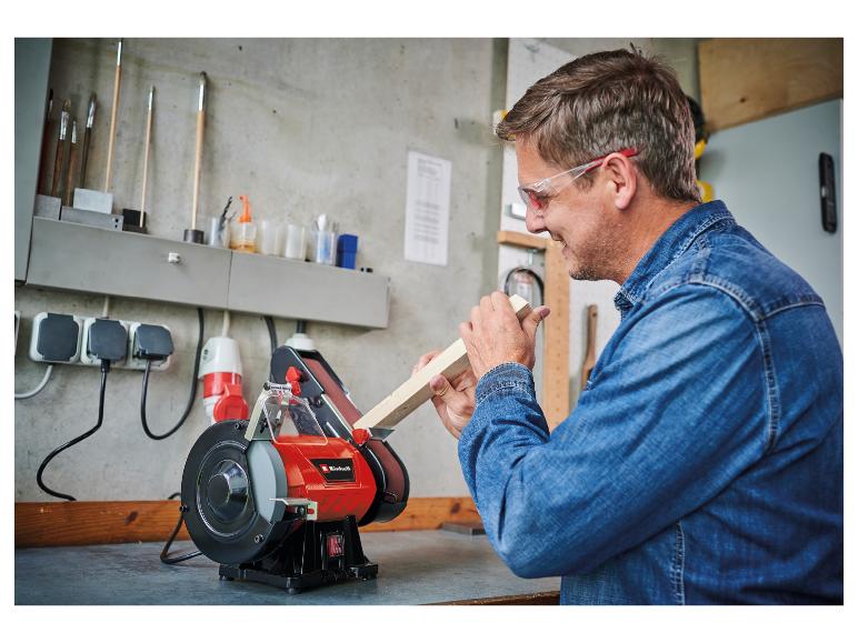 Mann schleift Holz an einer Schleifmaschine in der Werkstatt, mit Schutzbrille.