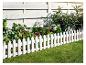 Weißer Zaun mit Spitzen entlang eines grünen Gartens mit blühenden Pflanzen.