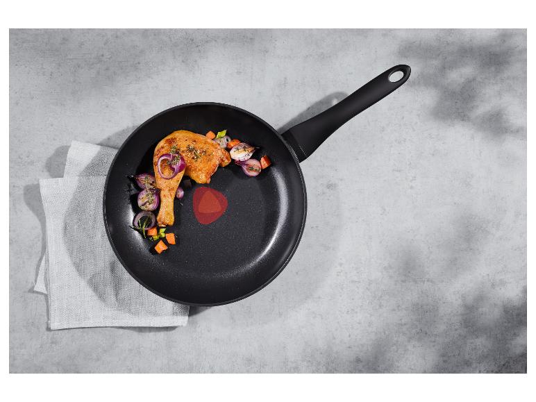 Gebratenes Hähnchenschenkel und Gemüse in einer schwarzen Pfanne auf einer Betonarbeitsplatte.