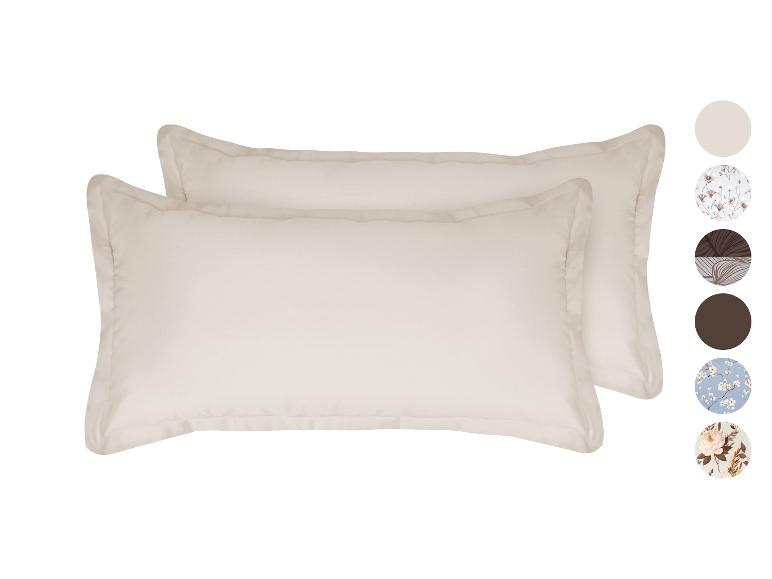 Zwei beige Kissen mit Zierrand und farbigen Stoffmustern an der Seite.