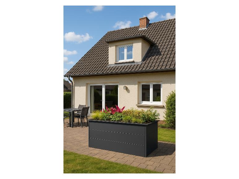 Großer Pflanzkübel mit bunten Pflanzen auf einer Terrasse mit Tisch und Stühlen vor einem Haus.