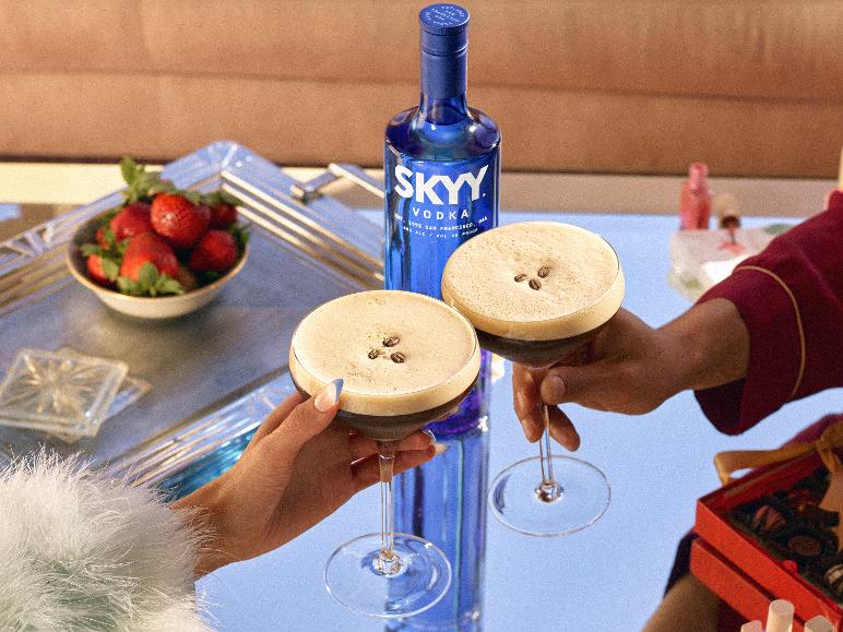 Zwei Espresso Martinis mit Kaffeebohnen, eine Flasche Wodka und eine Schale Erdbeeren.