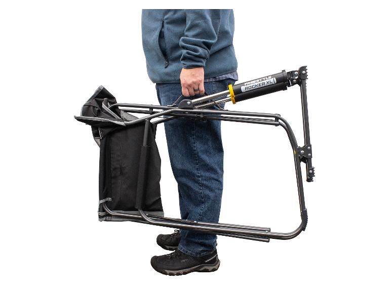 Ein Mann trägt einen zusammengeklappten Freestyle Rocker XL Campingstuhl.